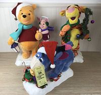 Full set of three animatronic figures from the Hundred Acre Wood in Christmas attire: Winnie the Pooh, Tigger, and Eeyore on snowy base with Christmas decorations.