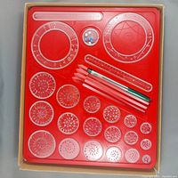Top-down view of the Spirograph set showing the red plastic tray containing numerous clear plastic gears and rings with teeth, four colored drawing pens, and a container with small colored pieces.