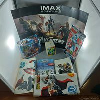 Photo of trading card packs, two card collection albums opened, loose cards stacked, and Avengers-themed posters including IMAX exclusive