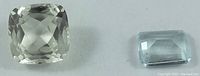 Photo showing two loose gemstones: a square cushion cut light green kunzite and a rectangular cut pale blue topaz.