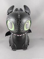 Front view of black Toothless dragon figurine with large green eyes that light up. Detailed texture on head and body.