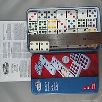 Top-down image showing the 28 double-9 domino tiles neatly arranged in a blue and red Pavilion branded case, along with a stainless steel ruler and instruction paper.
