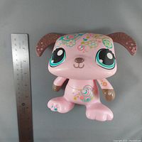 Front view of the pink dancing puppy figure with large blue eyes and floral decorations, placed next to a ruler for scale.