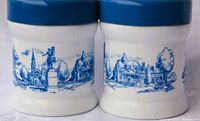Photo showing two white milk glass containers with blue plastic lids, decorated with blue American Revolutionary scenes including statues and colonial buildings.
