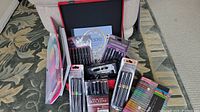 Photo showing Spectrum Noir marker sets, Studio Series skintone markers, and other marker pen sets in packaging inside a black and red art box.
