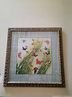 Framed silk embroidered butterfly artwork hanging on a wall, showing the full piece with mat and frame.