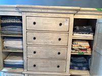 Front view of two whitewashed cabinets with drawers and open doors showing folded linens on shelves on both sides of central drawers
