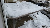 Rectangular glass-top table covered in snow on wooden deck