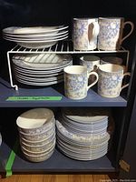 Overall view of cabinet shelf showing stacked plates and coffee mugs