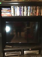 Closed cabinet showing the Samsung TV screen with remote control and electronics below, along with DVDs above.