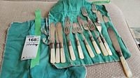 Full view of the cutlery set in green fabric roll-up holder showing 9 cutters and 9 forks with mother of pearl handles.