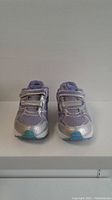 Front view of new Saucony kids running shoes size 3 showing the silver and lavender design with two Velcro straps each and light blue toe cap.