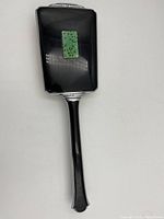 Photo of hand mirror showing front reflective surface, black handle with silver trim, and green carved decoration on back