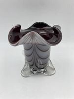 Top and angled views of a vintage art glass vase with curled ruffled rim, dark interior, and clear exterior decorated with white wave-like lines. Base has three raised feet.