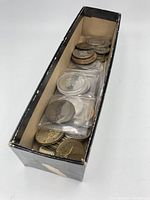View of the collection inside the black rectangular box showing a mix of coins and tokens stacked and some in plastic holders