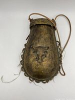 Front view of bronze shaman bag with embossed bull head, decorative edge loops, and leather strap placed flat on white background.