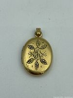 Front view of the oval gold fill locket showing engraved leaf and floral patterns with central script letter.