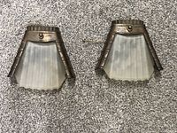 Pair of vintage wall sconces with ribbed frosted glass shades and aged metal frames showing patina and wear, laid on carpeted surface.