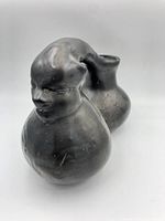 Side view of a Mexican black pottery jug with a sculpted human face and dual chamber design.