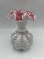 Front view of vintage milk glass vase with red fluted top and bead decoration on base.