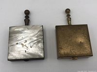 Top views of two square vintage ashtrays, one with mother of pearl lid and wooden handle, the other with brass-toned metal lid and metal handle.