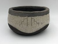 Side view photo showing Navajo pottery bowl with geometric stepped pattern engraved on off-white middle band, dark gray rim and brown base.