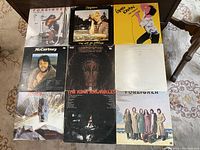 Top-down image showing nine vintage vinyl LP records on a table with varied album cover art and artist names.