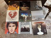 Top view of nine vintage vinyl record album covers arranged in a grid on a carpeted floor showing various artists and colorful designs.