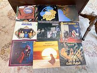 Top-down view of eight vintage vinyl albums on a dark wood surface, showing album covers with various artists and designs.