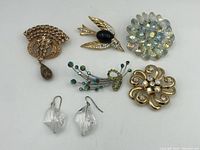Full lot arranged showing four brooches and one pair of earrings on white surface.