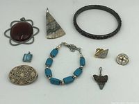 Photo shows assortment of sterling and costume jewelry including brooches, bracelets, pendants, and pins with abalone, turquoise stones, and various materials