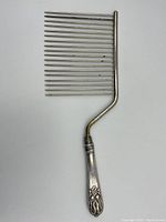 Front view of the whole comb showing floral handle and metal teeth.