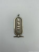Front view of the sterling silver pendant with detailed Egyptian hieroglyphic symbols on textured background inside cartouche shape.
