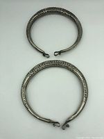 Top down view of two circular sterling silver tribal necklaces showing front engraved tribal designs and clasp hooks