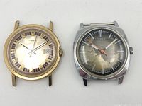 Two vintage Timex watches, one gold-tone round case with a date window, one silver-tone cushion case with aged dial and orange second hand.