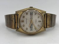 Close-up front view of Waltham watch showing dial with day and date display, gold tone case and metal band with wear and patina.