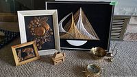 Photo showing assembled lot including framed copper repousse artworks of grapes and bear, string art sailboat, brass bowl, brass mouse ring holders, and barometer on carpet floor.