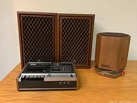 Sony stereo cassette player Model TC-121 in front with two Sansui mid-century speakers with fixed wooden diamond lattice grills behind, and Conference 2000 wood case speaker on right side.
