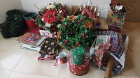 Wide view of entire lot showing artificial garland, floral centerpieces, electric candle centerpiece, various bags, songbooks, tins, gift wrap, and ornaments stacked on floor