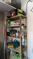Full view of the shelving unit with visible garden items on all shelves including pots, watering can, garden chemicals, and tools.