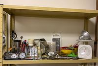 Full shelf view showing assorted kitchen tools including thermometers, peelers, scales, and presses arranged on a metal shelf