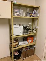 Full front view of beige metal shelving unit, filled with kitchen appliances and other household items. Shows 5 shelves and the general condition.