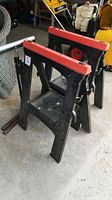Two black plastic folding saw horses with red tops placed side by side on the floor.