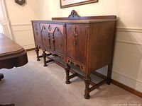 Angled side view showing carved details, turned legs and drawer/cabinet layout