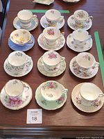 Twelve different teacups and matching saucers arranged on table showing variety of floral patterns and gold trim