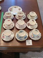 Overview photo showing nine teacups and saucers arranged on a table with Royal Albert 'Cosmos' plate at the back
