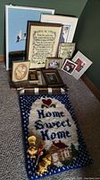View of assorted framed textile art pieces in various sizes and styles, with the largest frame approximately 21x17 inches. Included in the lot are framed cross stitch, needlepoint, and miniature art along with a latch hook rug and dough dolls.