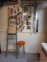 Full view of utility ladder, upholstered stool, and hand tools arranged on pegboard.
