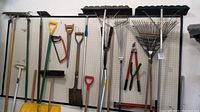 Front wall view of assorted yard tools including rakes, shovels, pruners hanging on pegboard