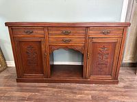 Front view of the antique wooden sideboard buffet showing three drawers on top, two carved doors below, and a central open space.